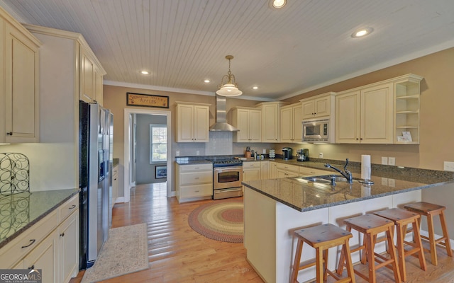 kitchen with kitchen peninsula, a kitchen breakfast bar, stainless steel appliances, sink, and wall chimney range hood