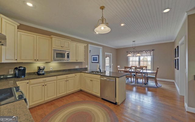 kitchen with kitchen peninsula, cream cabinets, stainless steel appliances, and decorative light fixtures