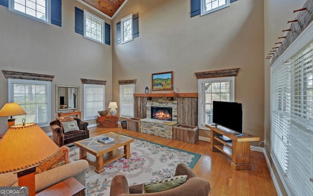 living room featuring a high ceiling, light wood-type flooring, a stone fireplace, and plenty of natural light