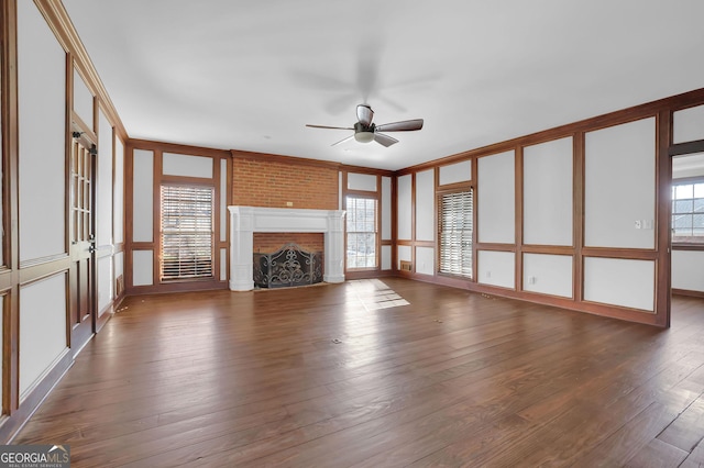 unfurnished living room with a large fireplace, plenty of natural light, dark wood-type flooring, and ceiling fan