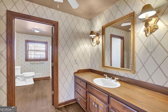 bathroom with hardwood / wood-style floors, vanity, ceiling fan, and toilet