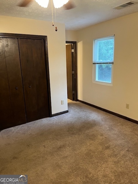 unfurnished bedroom featuring ceiling fan, a closet, light colored carpet, and a textured ceiling