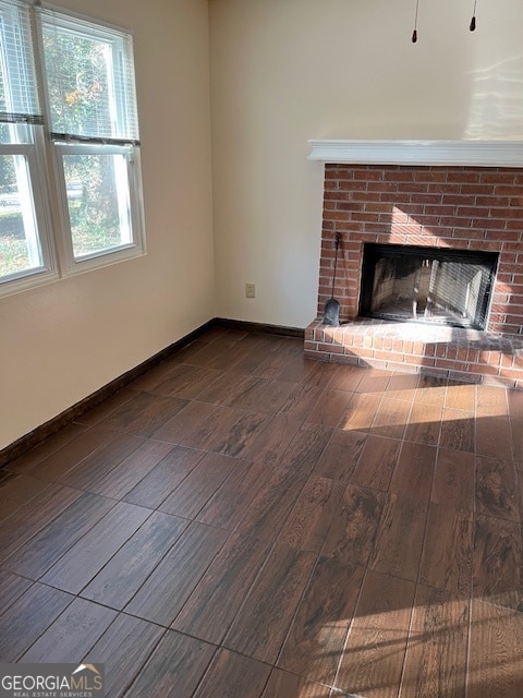 unfurnished living room with wood-type flooring, a brick fireplace, and plenty of natural light