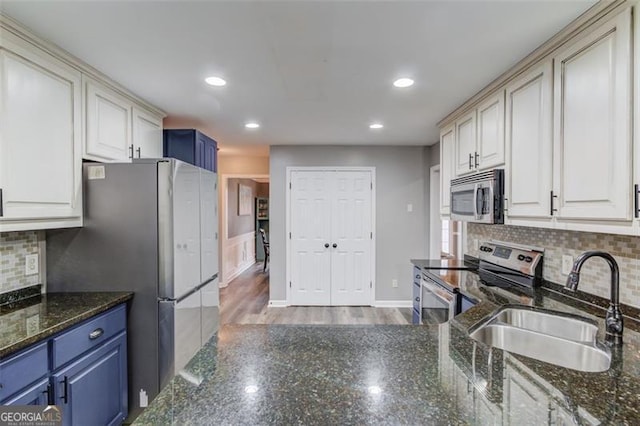 kitchen featuring appliances with stainless steel finishes, decorative backsplash, sink, blue cabinets, and dark stone counters