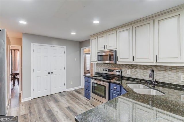 kitchen with appliances with stainless steel finishes, sink, blue cabinetry, dark stone counters, and decorative backsplash