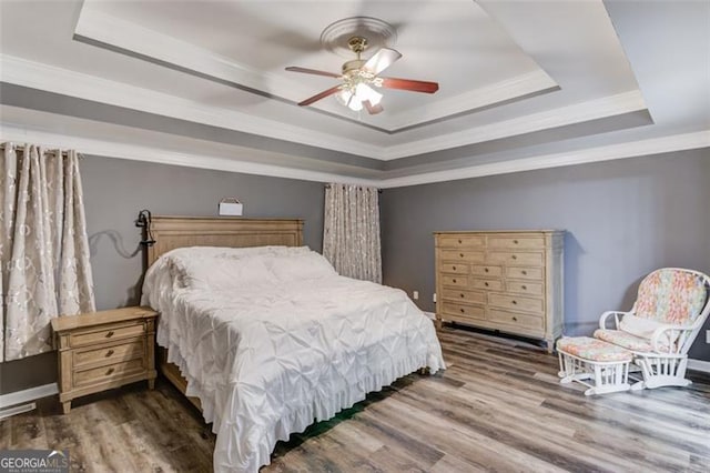 bedroom with ceiling fan, a raised ceiling, ornamental molding, and wood-type flooring