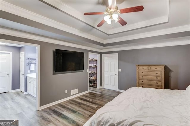 bedroom with ensuite bathroom, crown molding, wood-type flooring, a raised ceiling, and ceiling fan