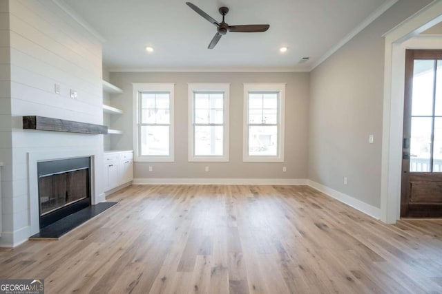 unfurnished living room with ceiling fan, a large fireplace, light wood-type flooring, and crown molding