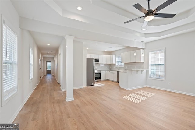 kitchen with light wood-type flooring, white cabinetry, hanging light fixtures, and backsplash