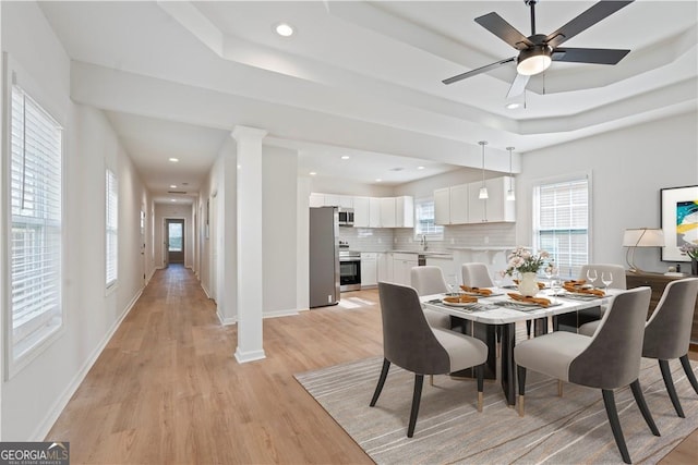 dining room with a raised ceiling, ceiling fan, and light hardwood / wood-style floors