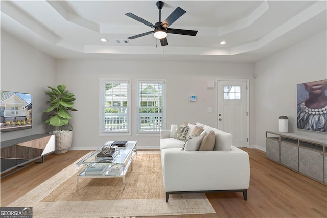 living room with a tray ceiling, light hardwood / wood-style flooring, and ceiling fan