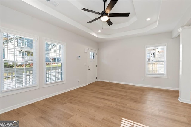 unfurnished room featuring light wood-type flooring, a raised ceiling, a wealth of natural light, and ceiling fan