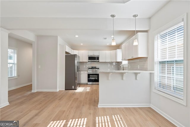 kitchen featuring white cabinets, stainless steel appliances, a breakfast bar area, and light hardwood / wood-style flooring