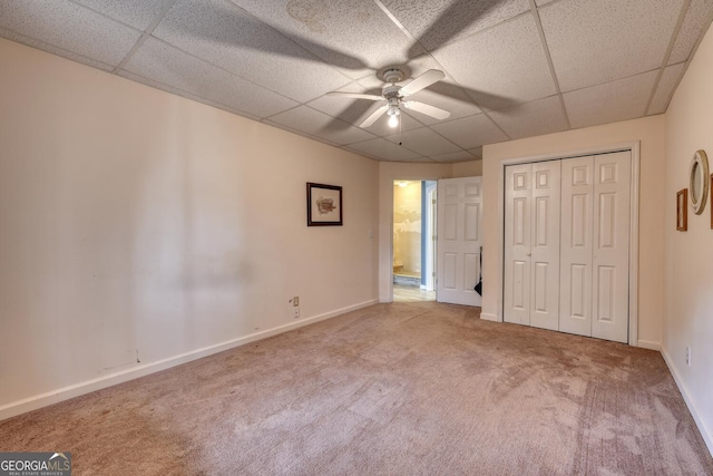 unfurnished bedroom with a paneled ceiling, ceiling fan, carpet floors, and a closet