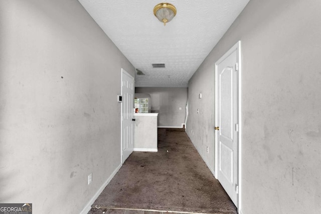 hallway featuring dark colored carpet and a textured ceiling