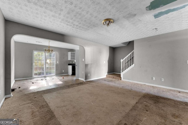 unfurnished living room with carpet flooring, a textured ceiling, and an inviting chandelier