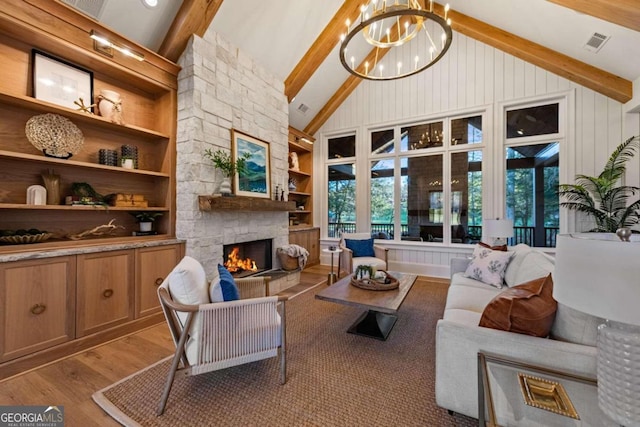 living room with built in shelves, light wood-type flooring, beamed ceiling, and a stone fireplace