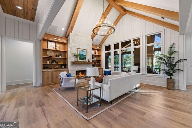 living room featuring a fireplace, beamed ceiling, an inviting chandelier, light wood-type flooring, and built in shelves