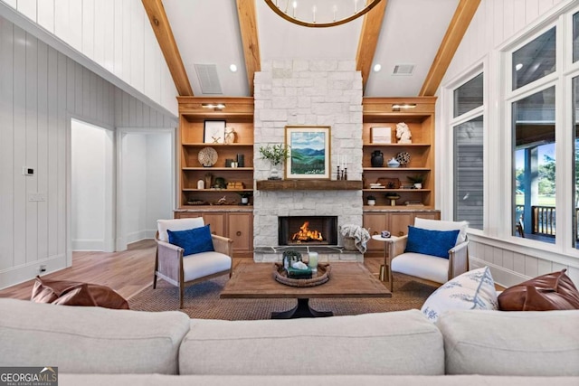 living room with light hardwood / wood-style floors, built in features, a stone fireplace, and lofted ceiling with beams