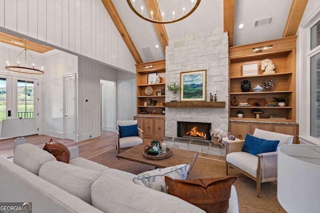 living room with built in shelves, a fireplace, light hardwood / wood-style floors, wood walls, and a notable chandelier