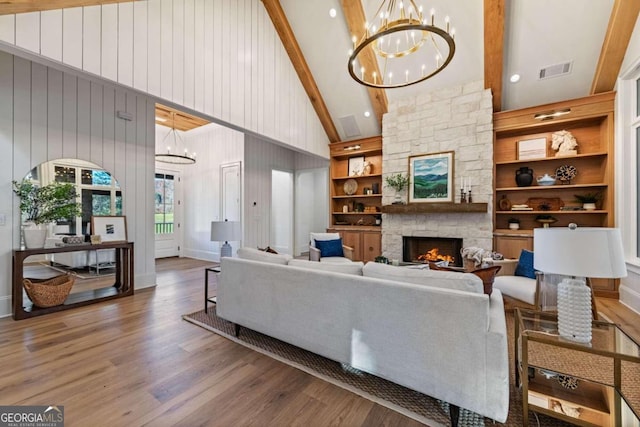 living room with an inviting chandelier, hardwood / wood-style floors, a fireplace, beam ceiling, and built in shelves