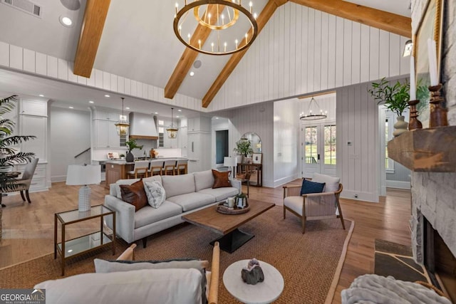 living room featuring light wood-type flooring, a fireplace, high vaulted ceiling, a chandelier, and beam ceiling