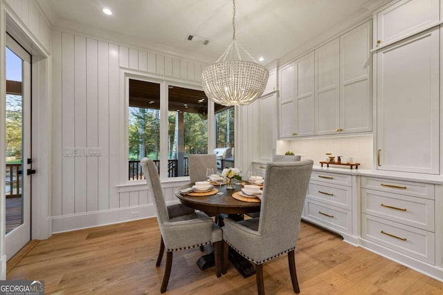 dining room featuring light wood-type flooring, ornamental molding, an inviting chandelier, and a healthy amount of sunlight