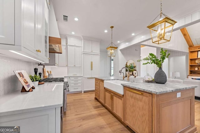 kitchen featuring white cabinets, gas stove, sink, hanging light fixtures, and a large island