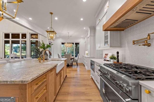 kitchen featuring white cabinets, custom exhaust hood, sink, stainless steel stove, and a center island with sink