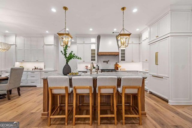 kitchen featuring a center island with sink, white cabinets, light hardwood / wood-style flooring, and custom range hood