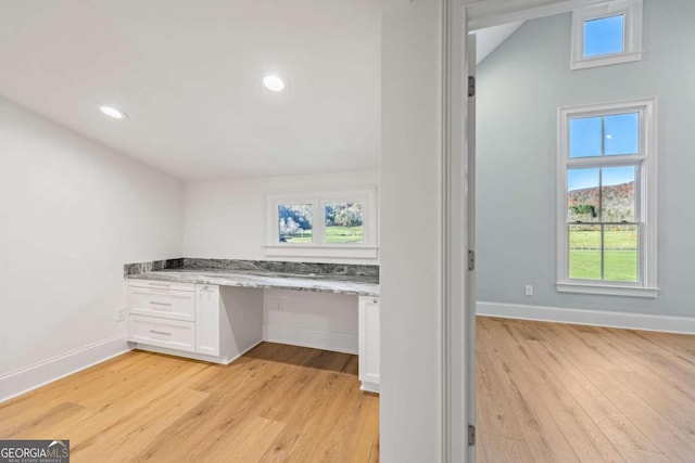 unfurnished office with built in desk, light wood-type flooring, and lofted ceiling