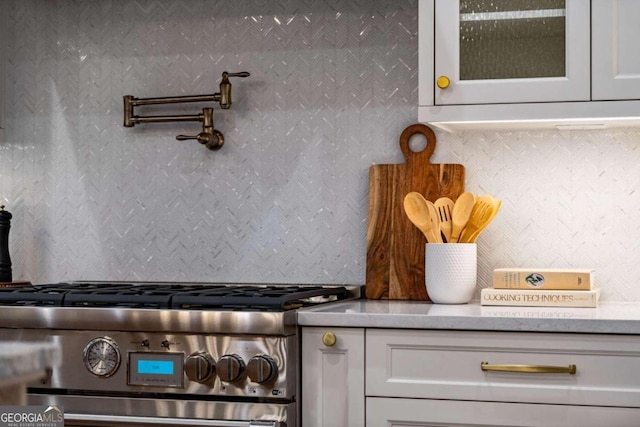 interior details with white cabinets, decorative backsplash, and high end range