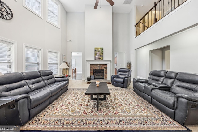 living room featuring a towering ceiling, a stone fireplace, plenty of natural light, and ceiling fan