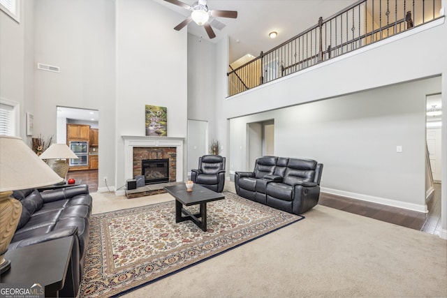 living room featuring a fireplace, a high ceiling, ceiling fan, and wood-type flooring