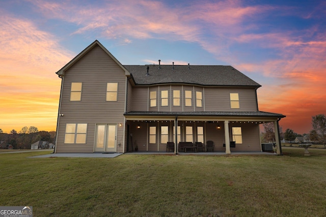 back house at dusk with a lawn, a patio area, and central AC