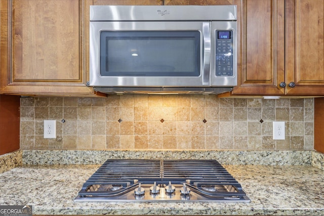 kitchen with backsplash, light stone counters, and stainless steel appliances