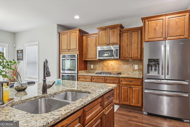 kitchen with sink, dark hardwood / wood-style floors, decorative backsplash, light stone countertops, and appliances with stainless steel finishes