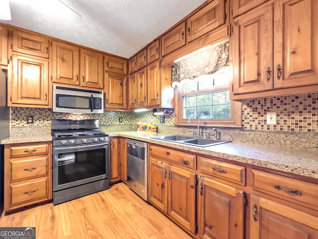 kitchen with sink, stainless steel appliances, backsplash, light hardwood / wood-style floors, and a textured ceiling