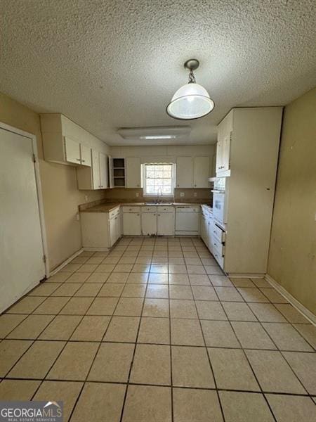 kitchen featuring sink, white oven, white cabinets, a textured ceiling, and light tile patterned floors