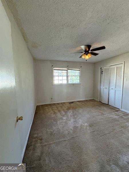 unfurnished bedroom with carpet, ceiling fan, a textured ceiling, and a closet