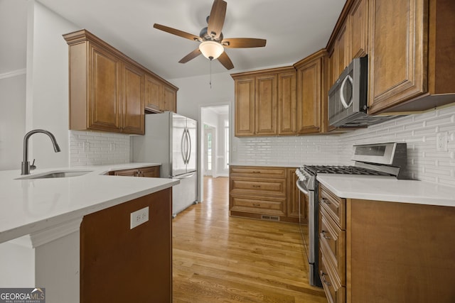 kitchen featuring decorative backsplash, a ceiling fan, light wood-style floors, a sink, and stainless steel appliances