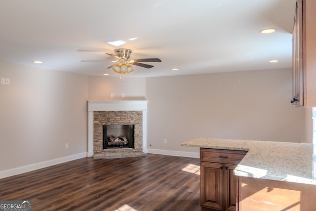 unfurnished living room with dark hardwood / wood-style floors, ceiling fan, and a stone fireplace