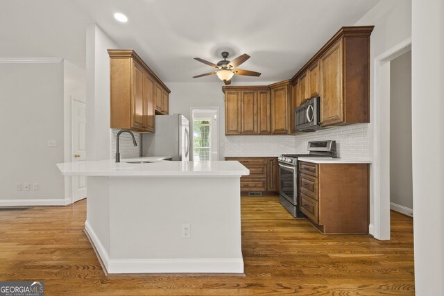 kitchen with ceiling fan, backsplash, a sink, a peninsula, and stainless steel appliances