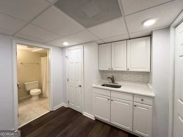 bar with a drop ceiling, backsplash, dark wood-type flooring, white cabinets, and sink