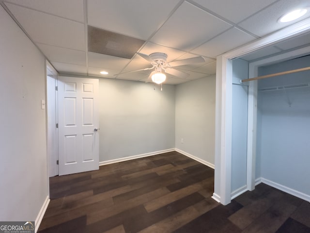 basement with ceiling fan, a drop ceiling, and dark wood-type flooring