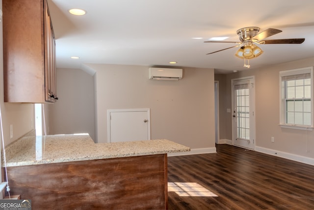 kitchen with dark hardwood / wood-style floors, ceiling fan, a wall mounted AC, light stone counters, and kitchen peninsula