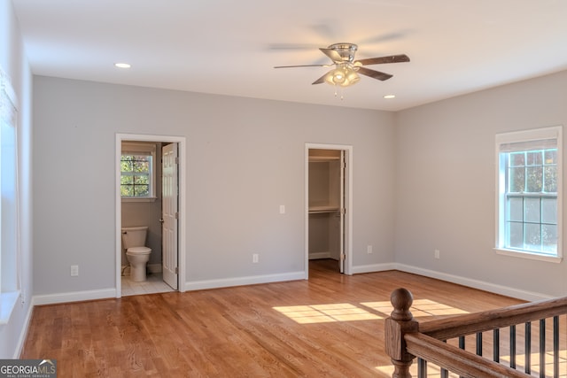 unfurnished bedroom with ensuite bath, ceiling fan, a spacious closet, light hardwood / wood-style floors, and a closet