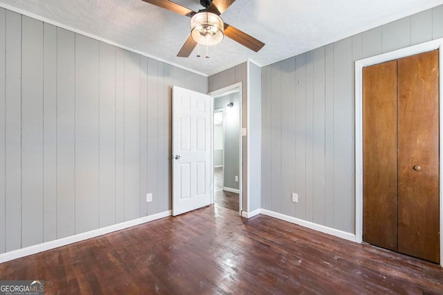 unfurnished bedroom featuring ceiling fan, a closet, dark wood-type flooring, and wood walls