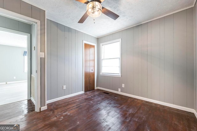 empty room featuring a textured ceiling, dark hardwood / wood-style flooring, and wooden walls