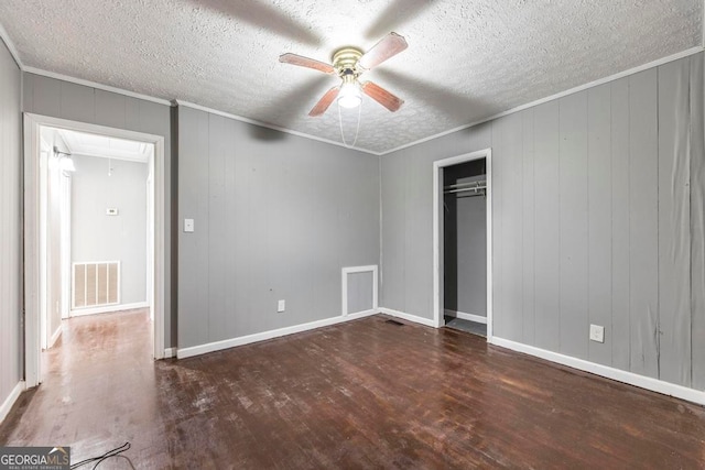 unfurnished bedroom with dark hardwood / wood-style flooring, ornamental molding, a textured ceiling, ceiling fan, and wooden walls